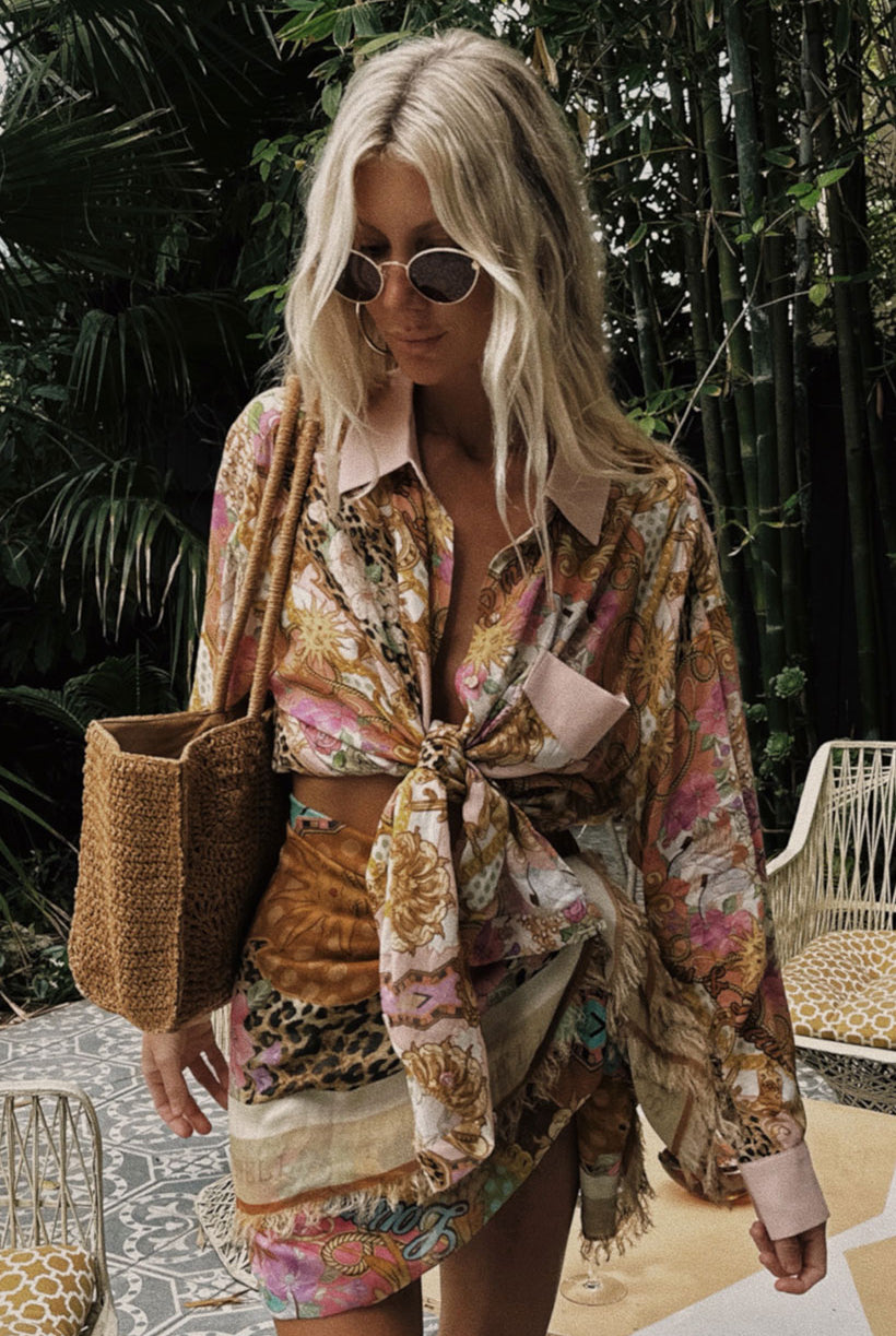 Woman in a patterned shirt and skirt standing outdoors with plants in the background