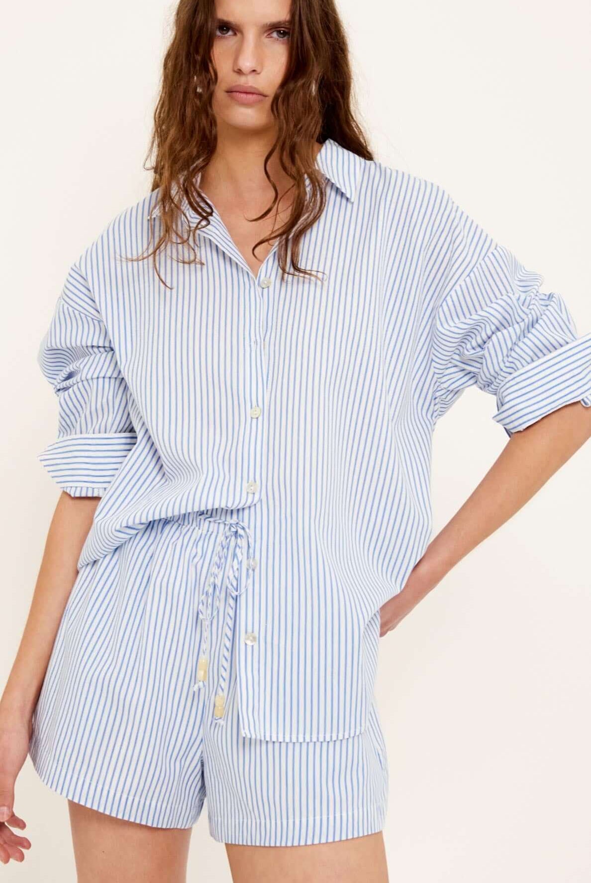 Woman wearing a blue and white striped shirt and shorts set on a white background