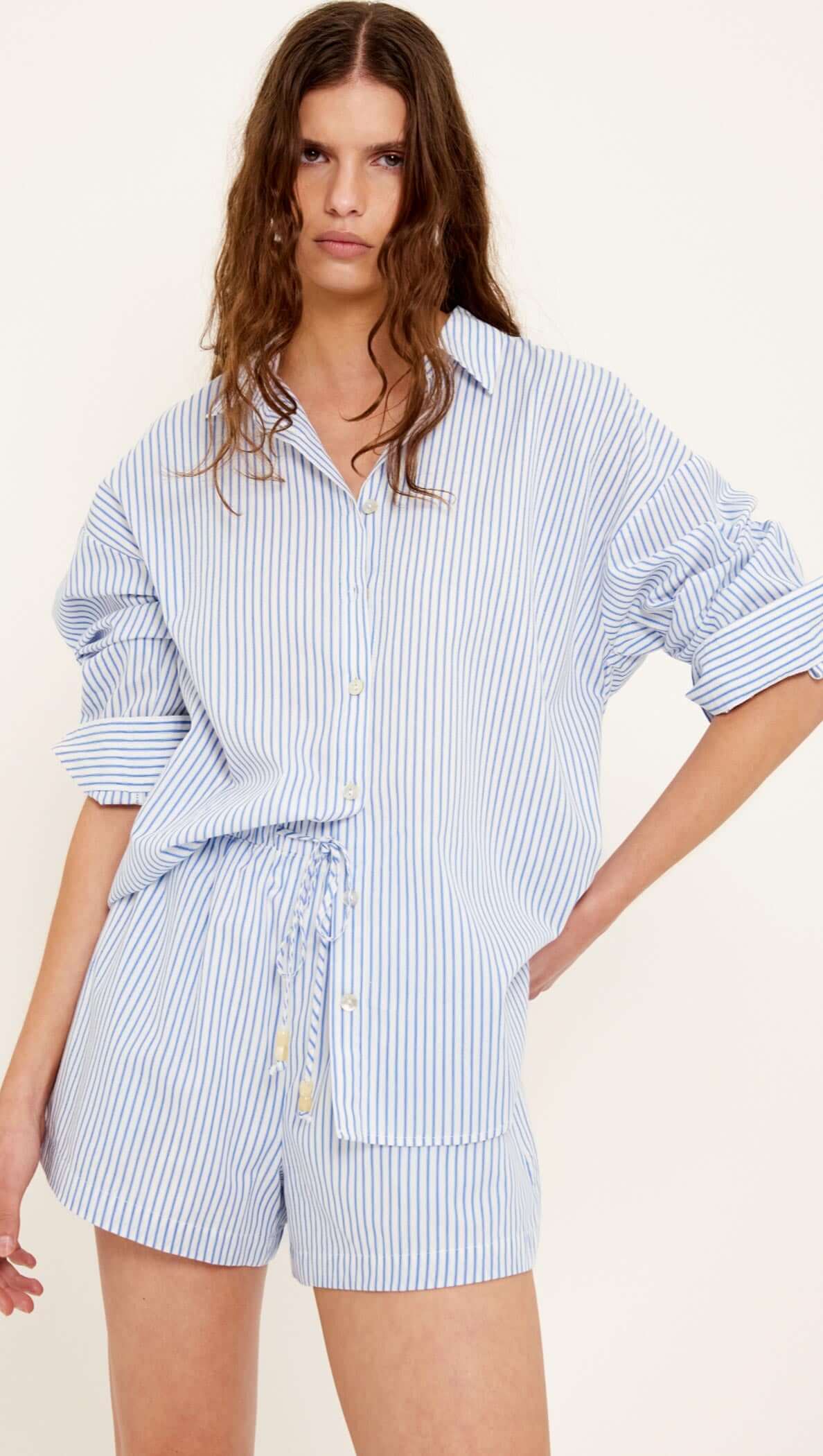 Woman wearing a blue and white striped shirt and shorts set on a white background