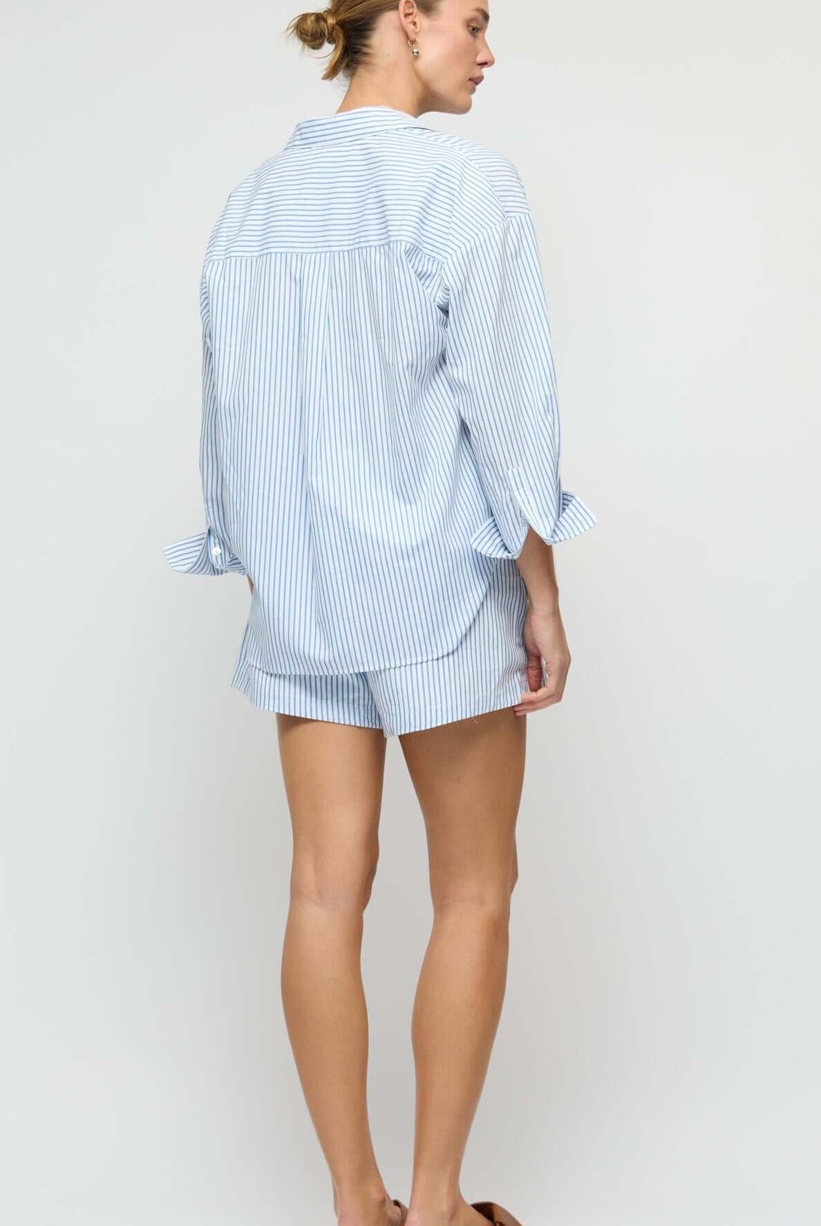 Woman wearing a light blue striped shirt and shorts on a white background