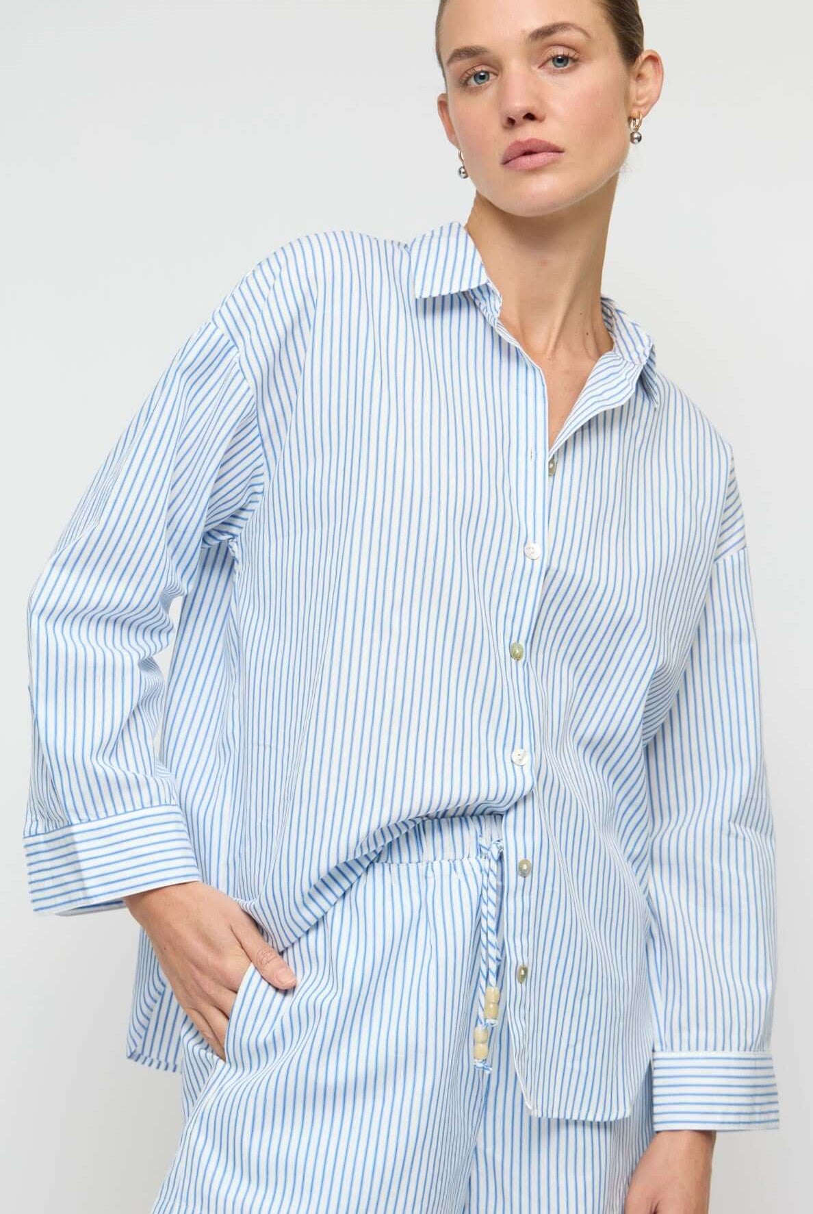 Woman wearing a blue and white striped shirt and shorts set against a plain background