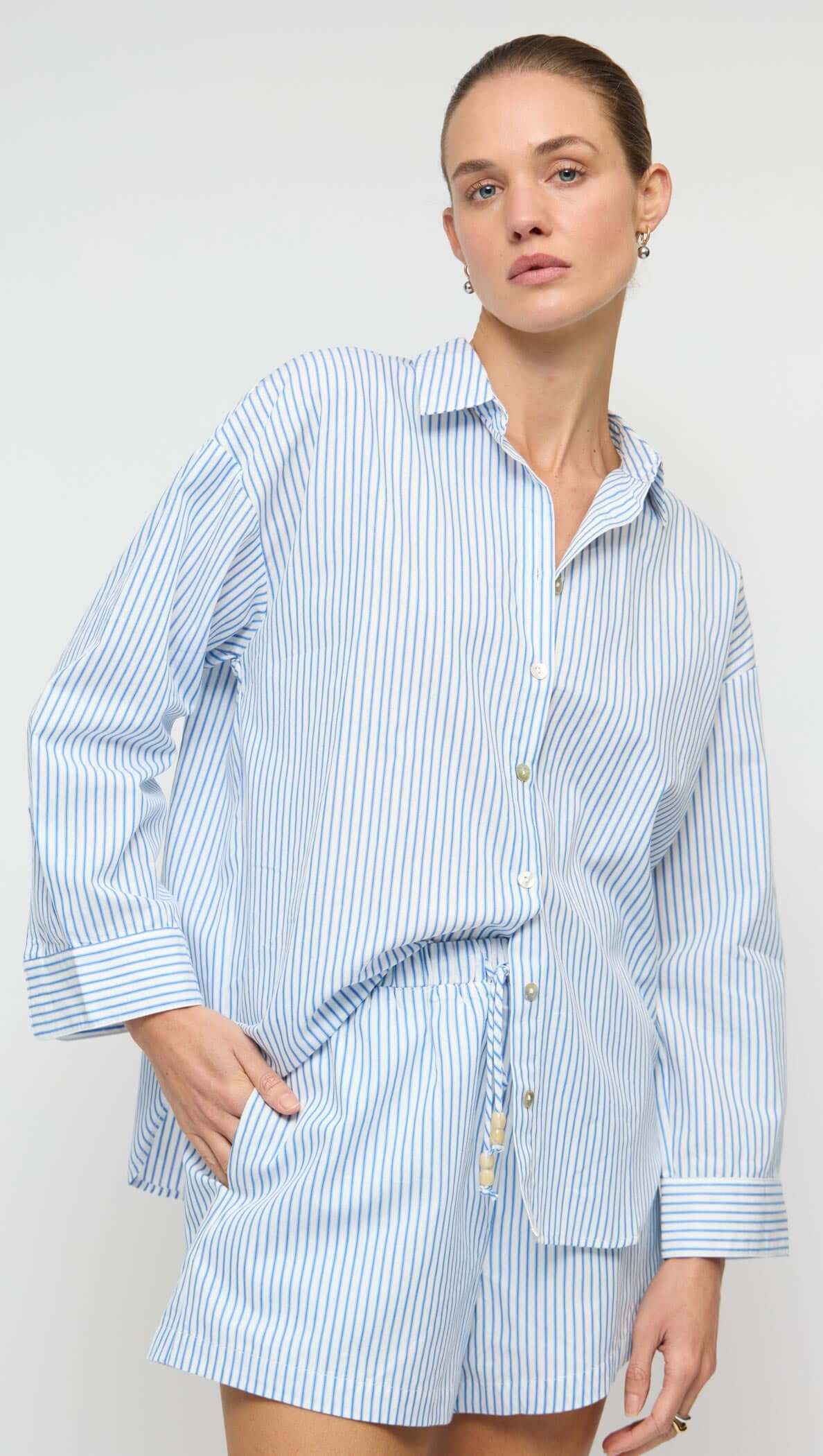 Woman wearing a blue and white striped shirt and shorts set against a plain background