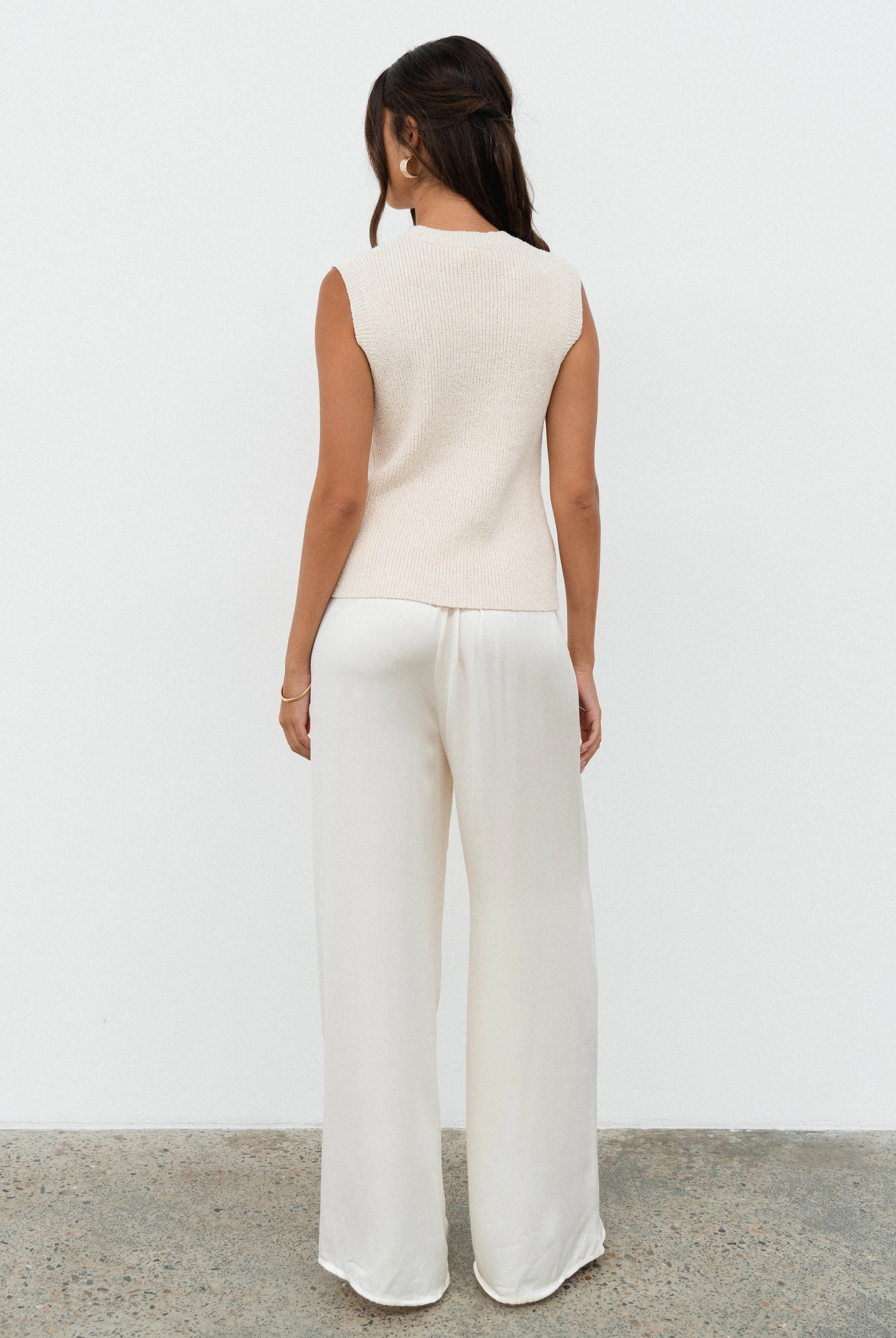 Woman wearing a white sleeveless top and wide-leg pants against a plain background