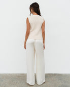 Woman wearing a white sleeveless top and wide-leg pants against a plain background