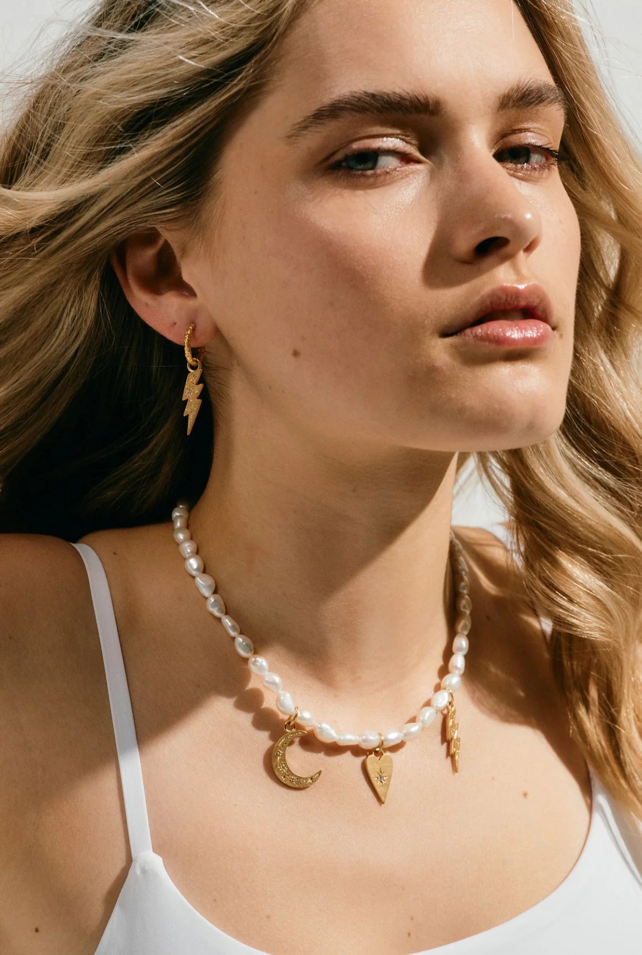 Woman wearing a pearl necklace with gold charms against a neutral background