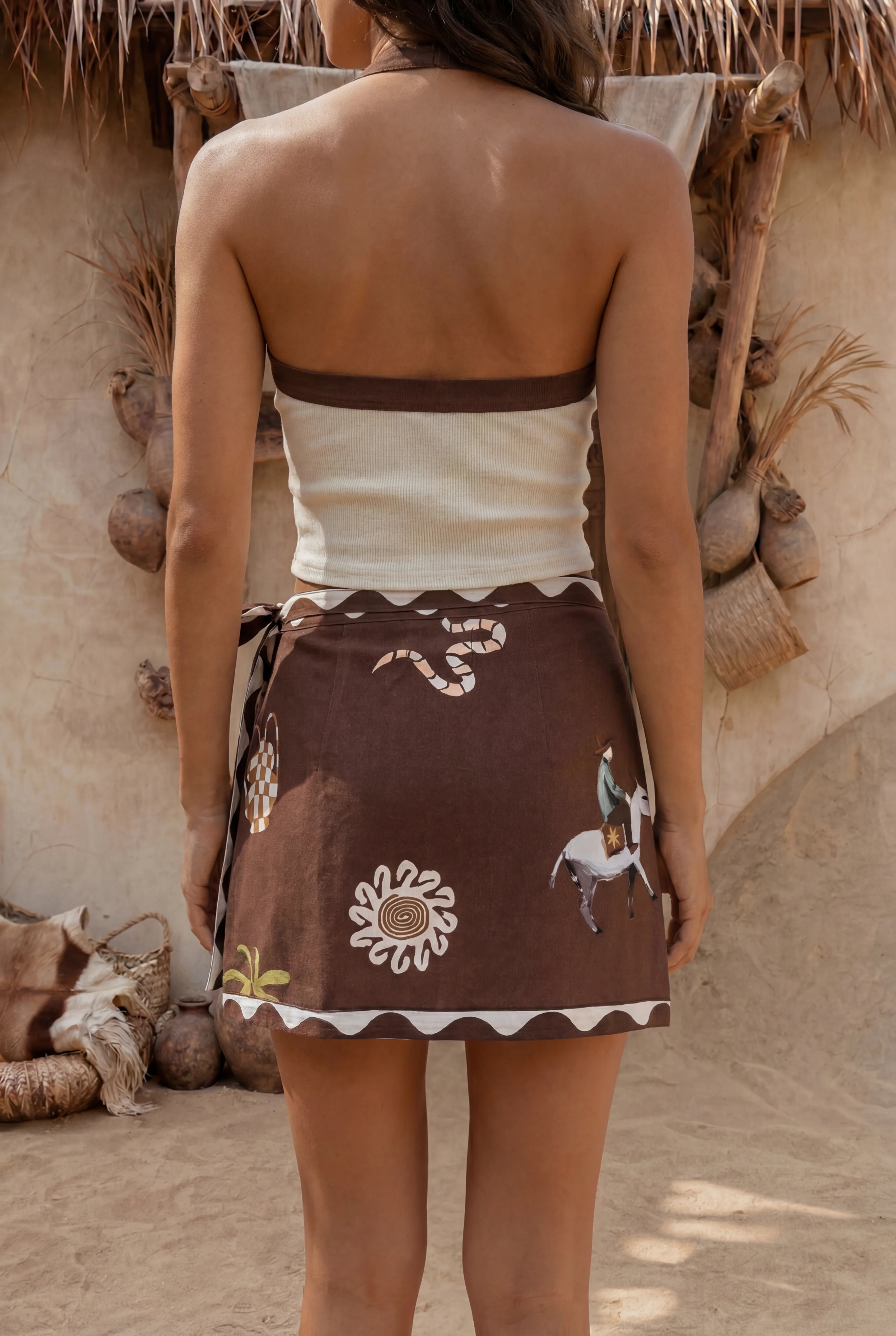 Person wearing a traditional brown and white outfit with floral patterns in front of a rustic wall.