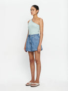 Woman wearing mint one shoulder tank and lightwash denim shorts