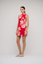 Woman wearing a red dress with white floral pattern on a plain background