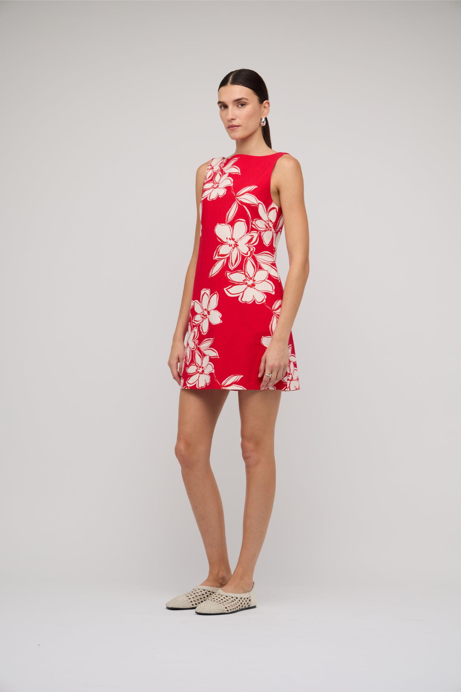 Woman wearing a red dress with white floral pattern on a plain background