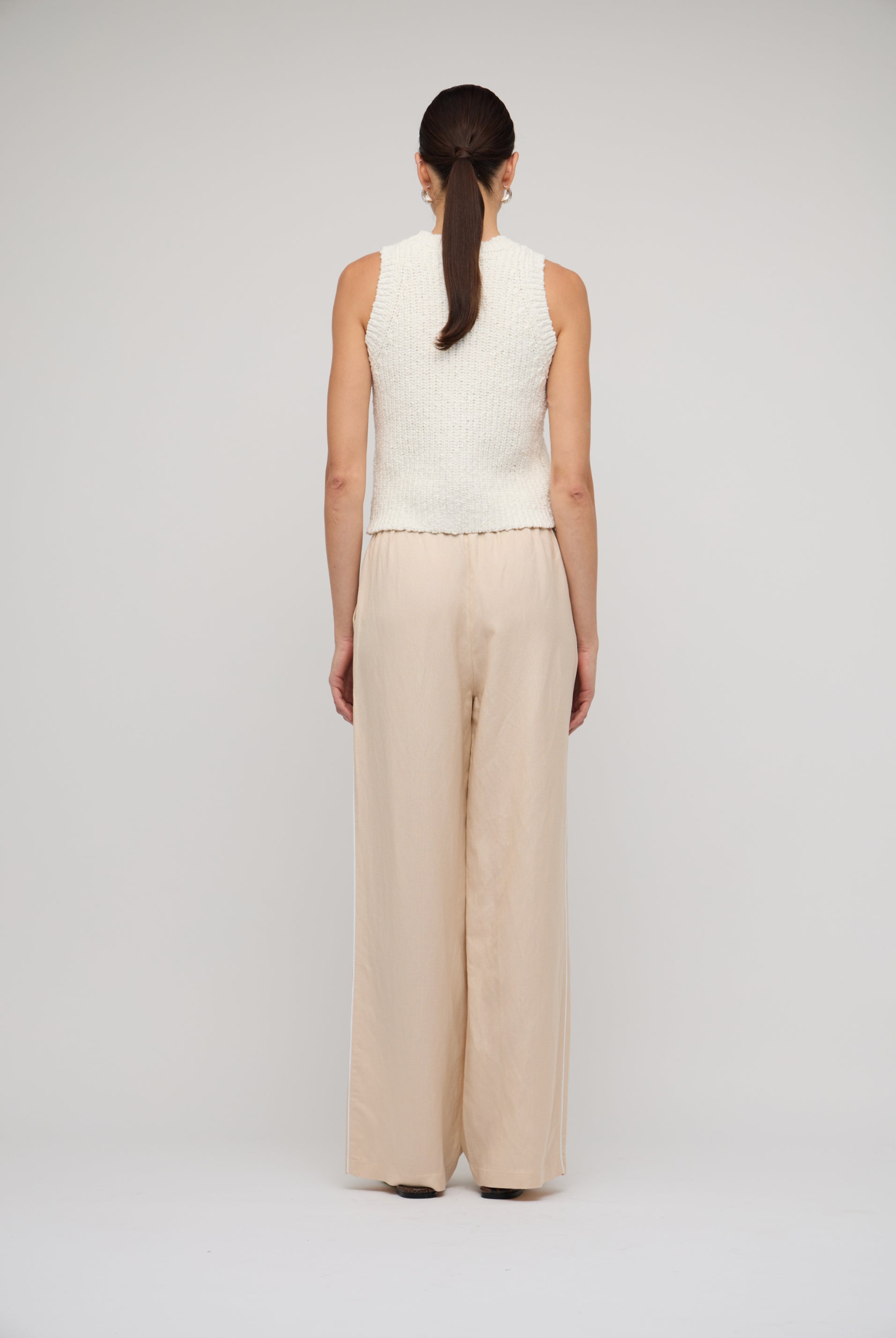 Person wearing a white sleeveless top and beige wide-leg pants on a light gray background