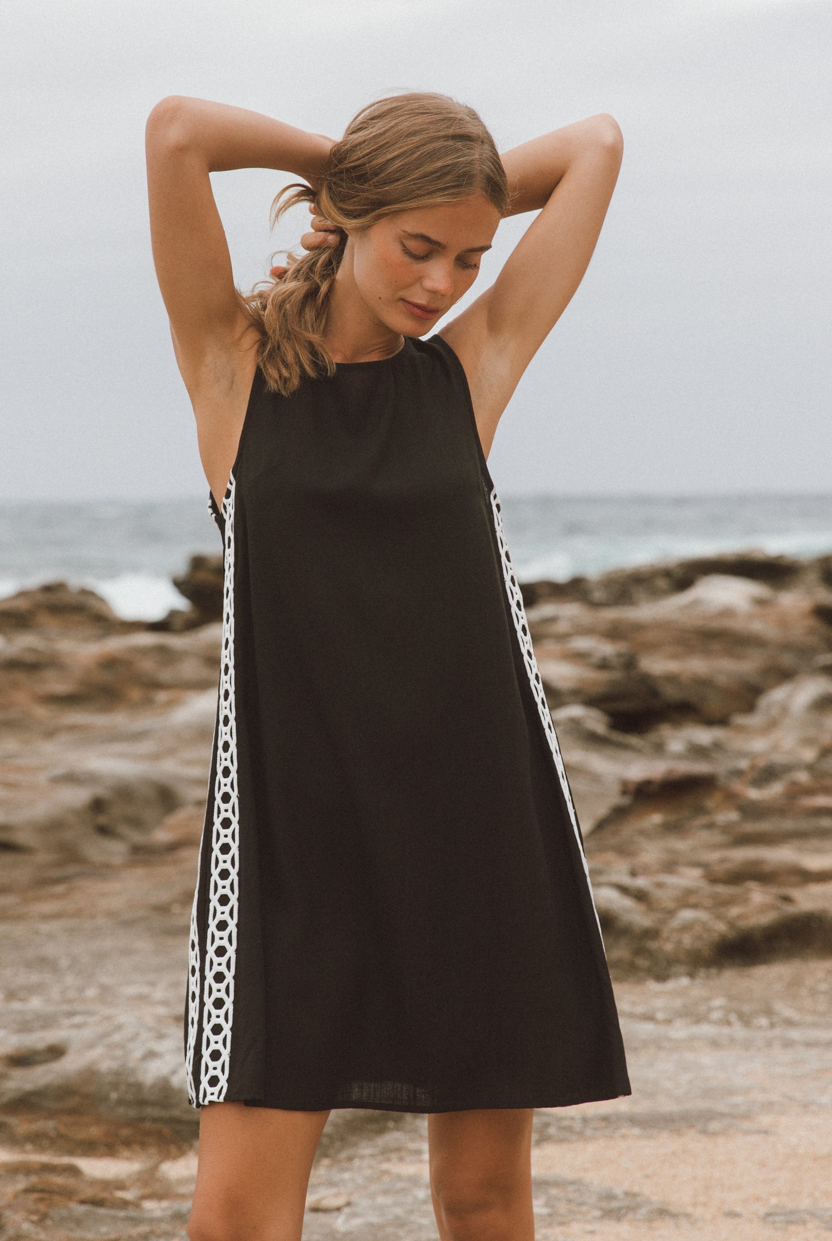 Woman wearing a black dress with white trim on a rocky beach.