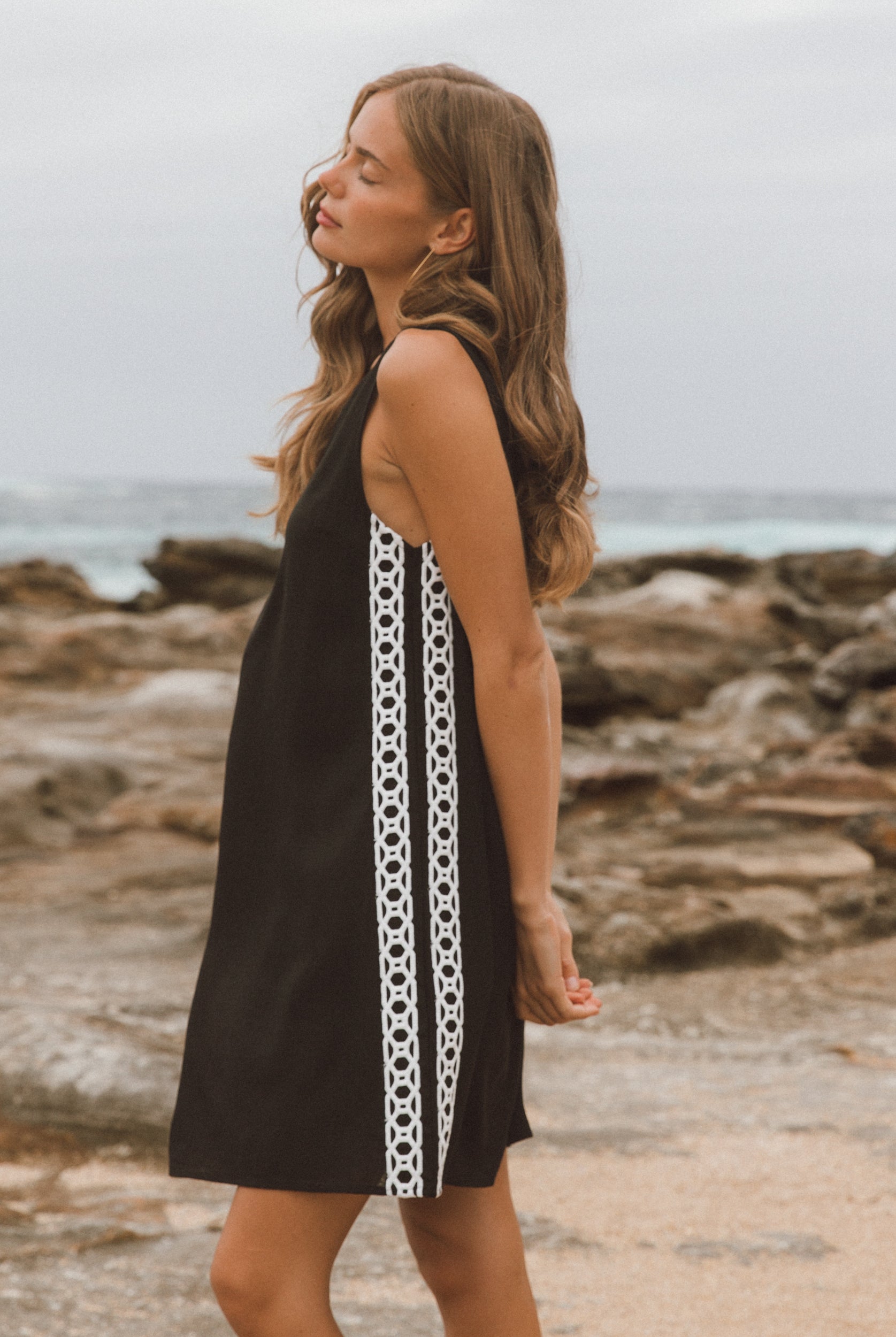 Woman wearing a black dress with white pattern on a rocky beach