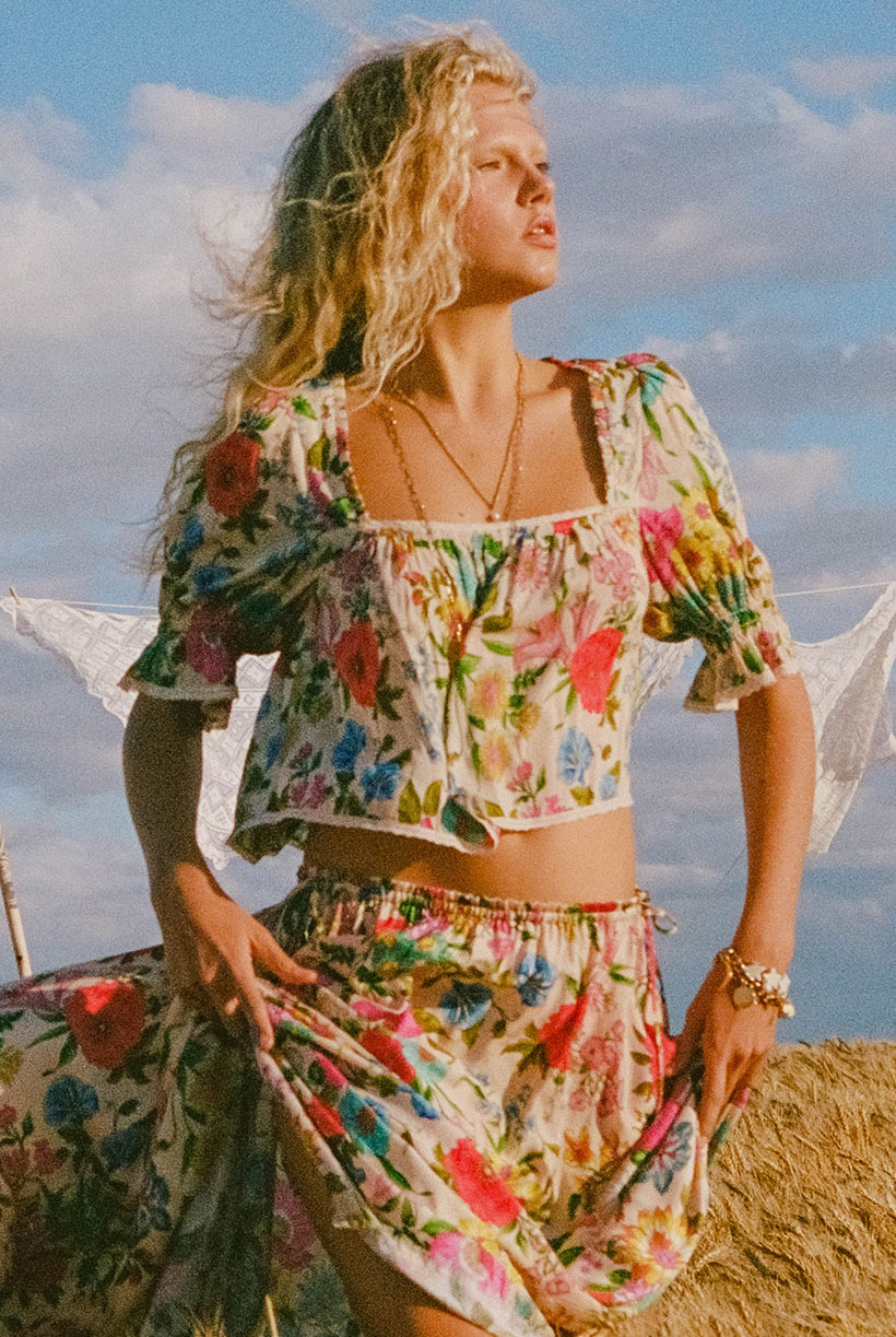 Woman in a floral outfit standing outdoors with a blue sky and clouds in the background
