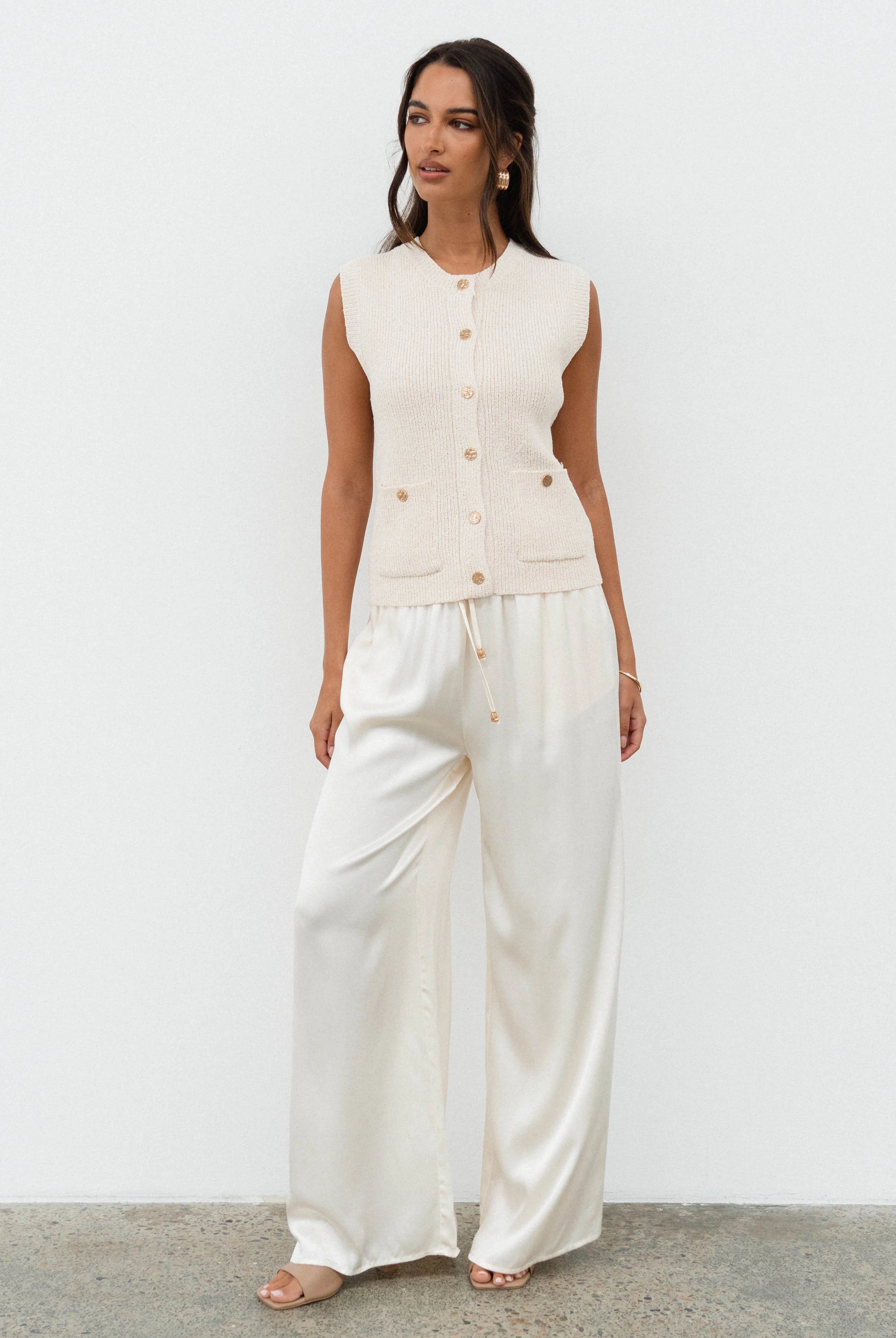Woman wearing a white sleeveless top and wide-leg pants against a plain background