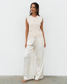 Woman wearing a white sleeveless top and wide-leg pants against a plain background