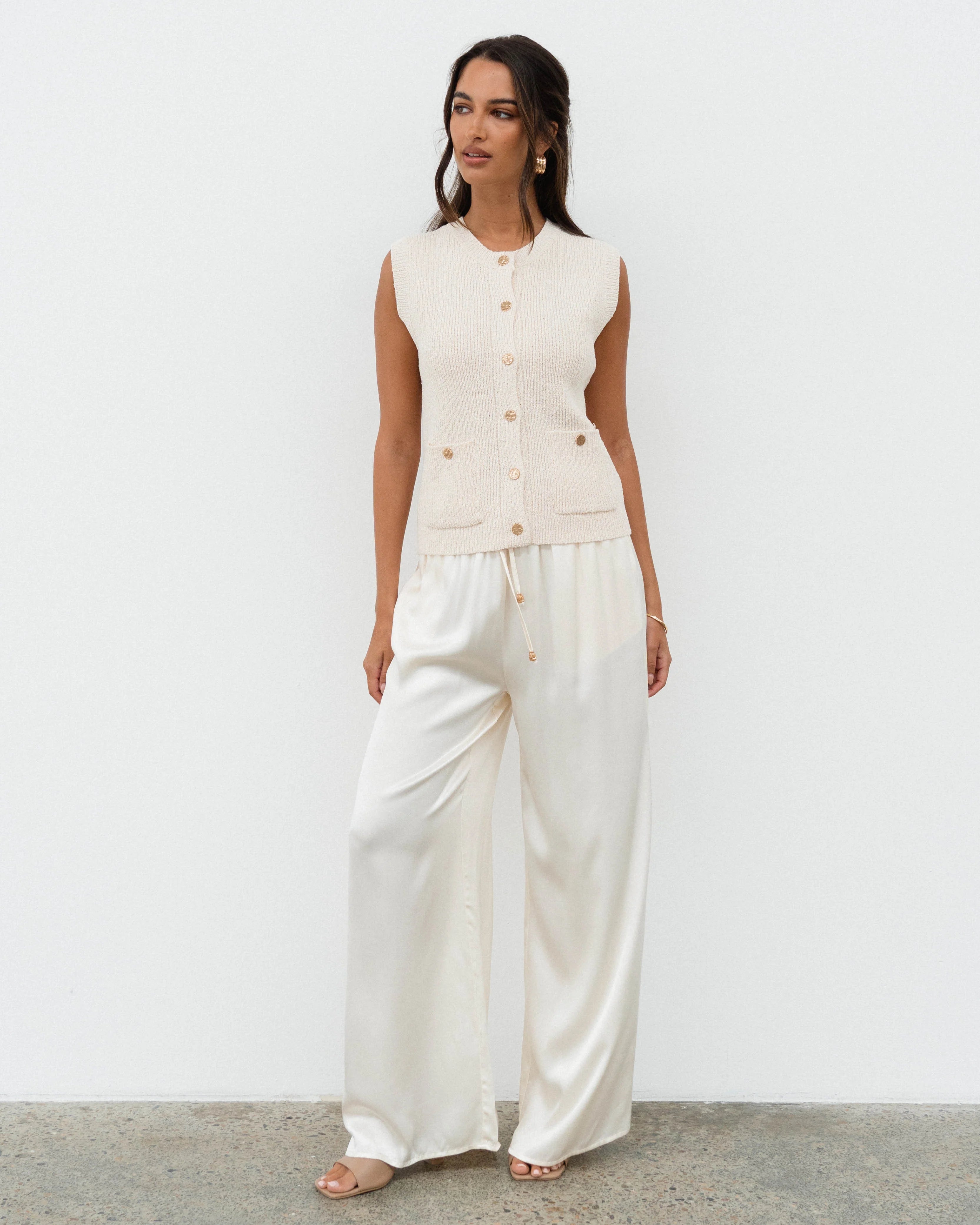 Woman wearing a white sleeveless top and wide-leg pants against a plain background