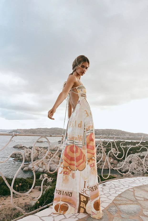 Woman in a floral dress standing by a scenic coastal area with a cloudy sky.