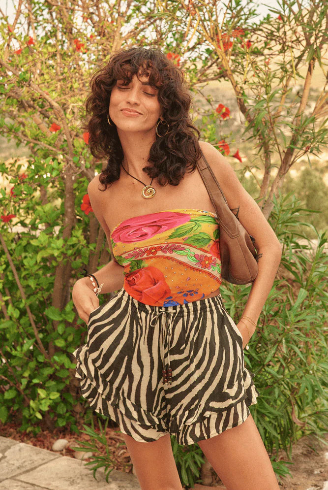 Woman wearing a colorful top and zebra print shorts standing in a garden.
