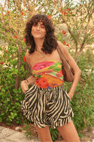 Woman wearing a colorful top and zebra print shorts standing in a garden.