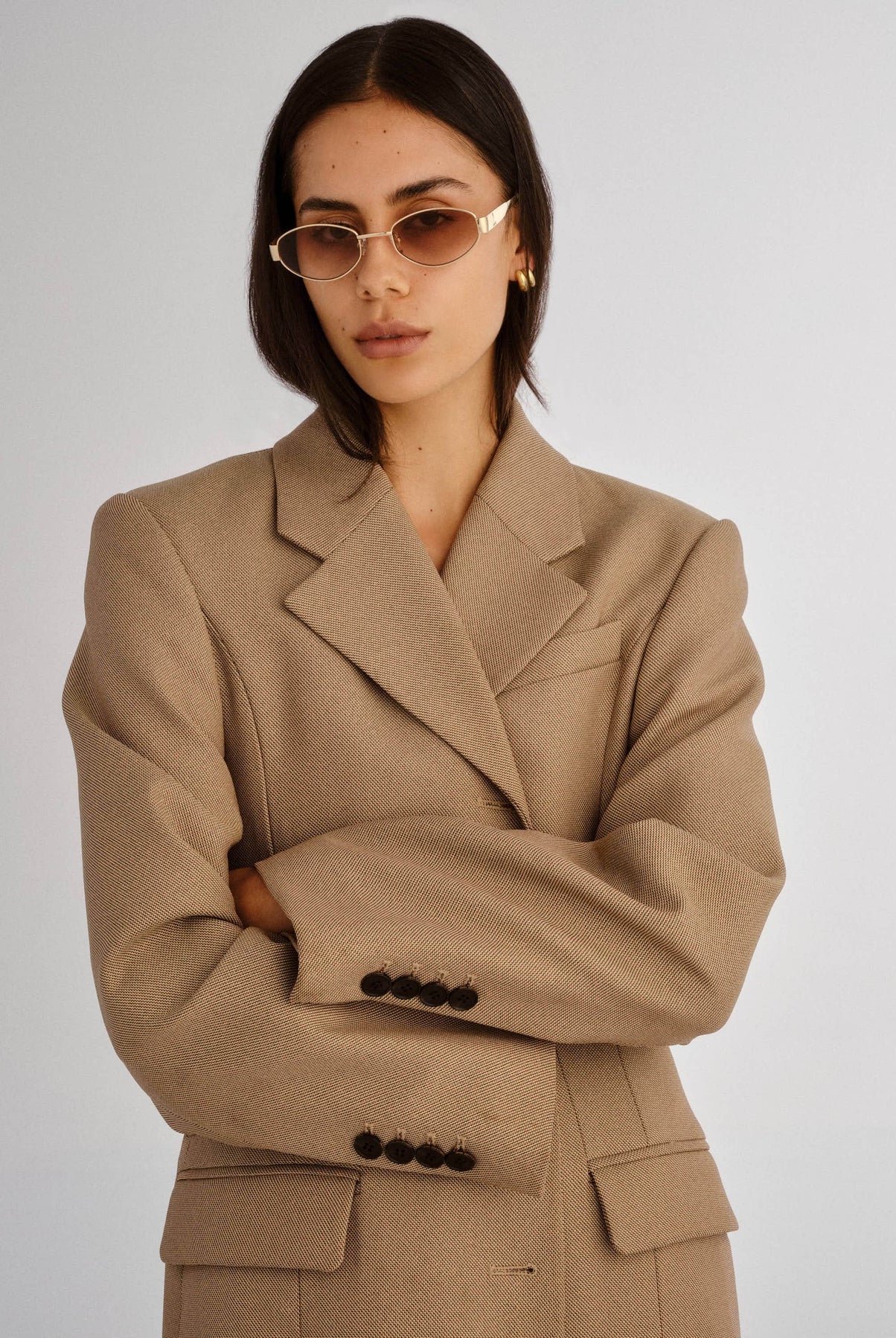 Woman wearing a beige suit with sunglasses on a plain background