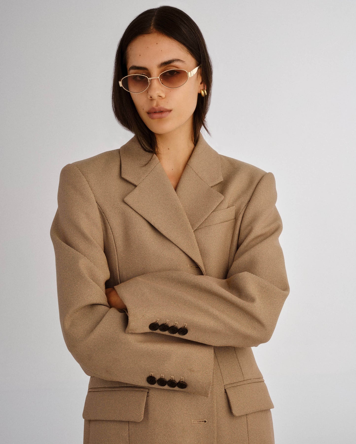 Woman wearing a beige suit with sunglasses on a plain background