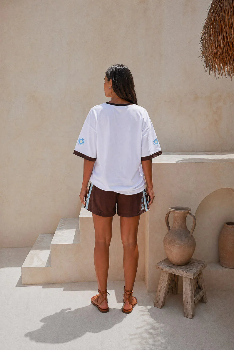 Person wearing a Palm Collective Maroc t-shirt in white with brown sleeve trim and brown and blue decorations