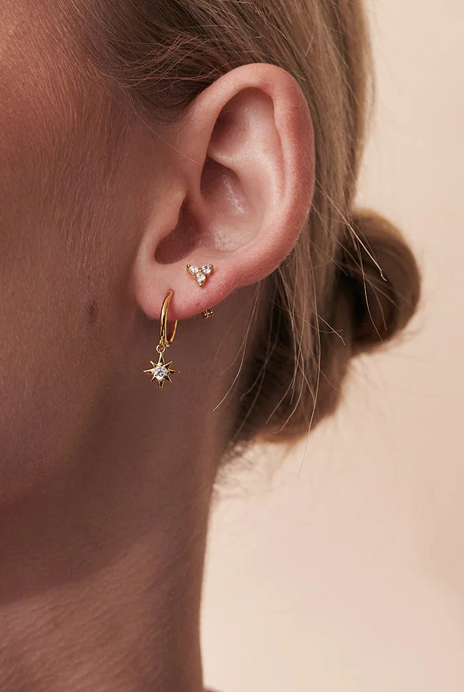 Close-up of a person wearing gold hoop earrings with small diamonds on a beige background