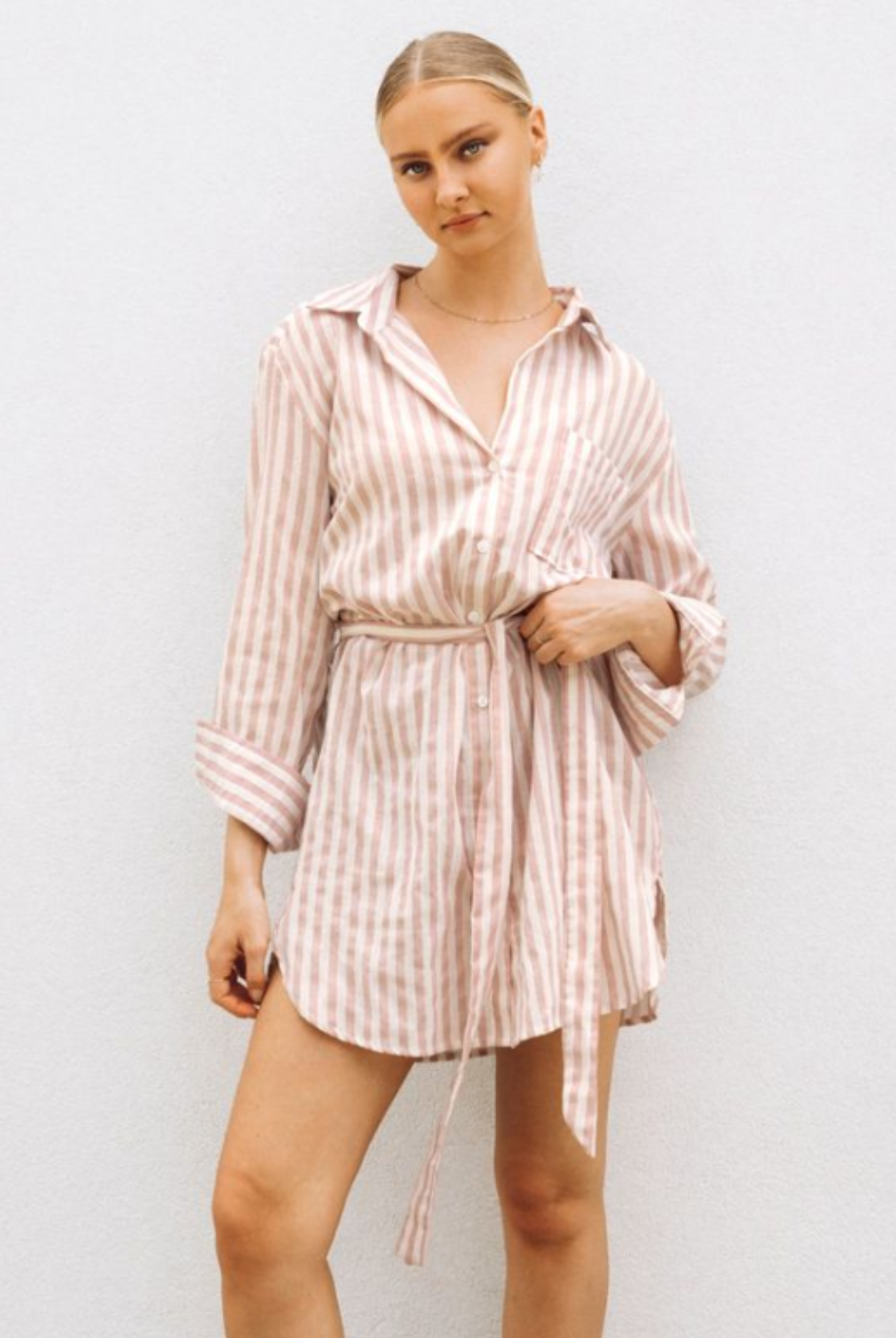 Model wearing soft pink stripe shirt dress with functional button placket, collar and belt