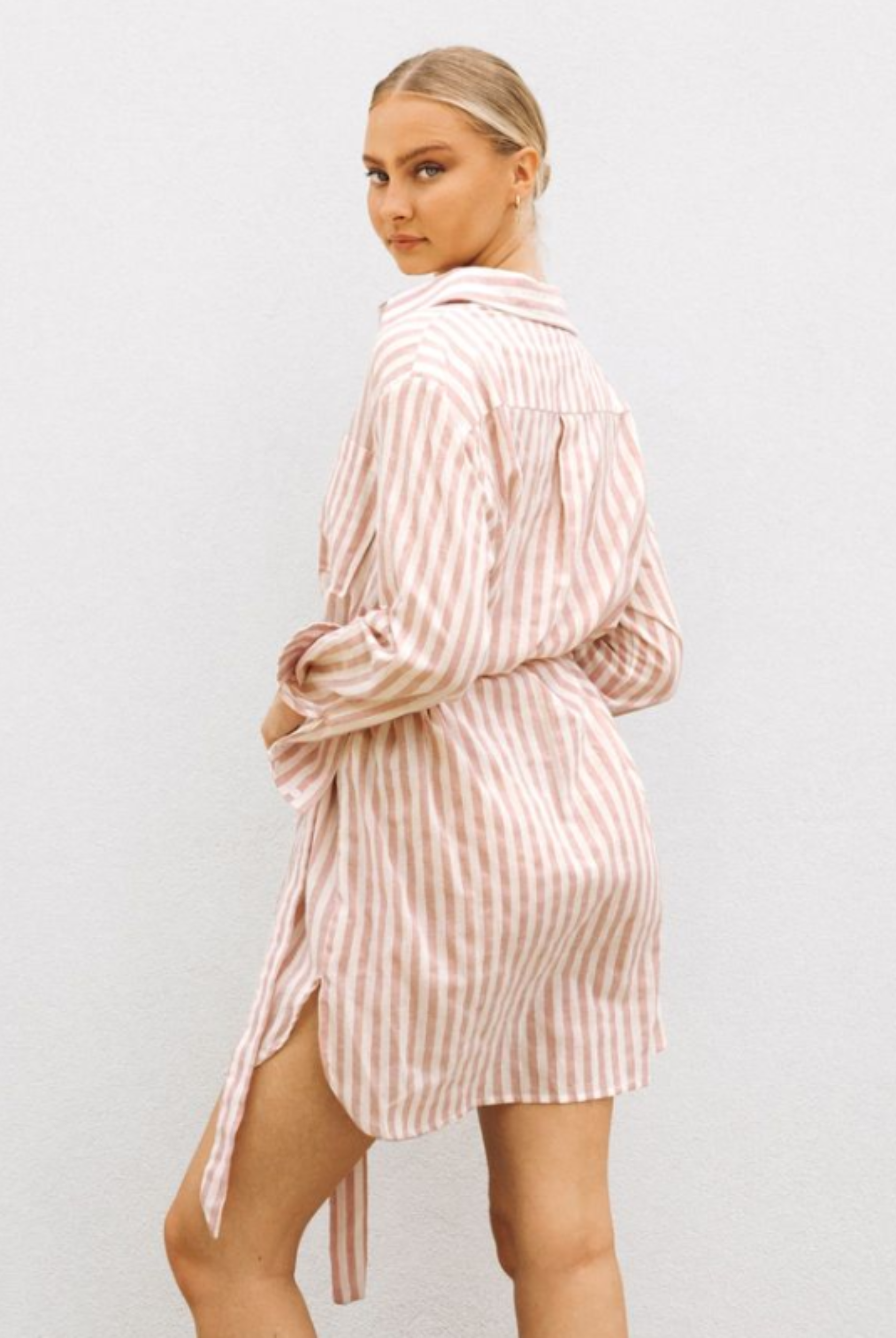 Model wearing soft pink stripe shirt dress with functional button placket, collar and belt