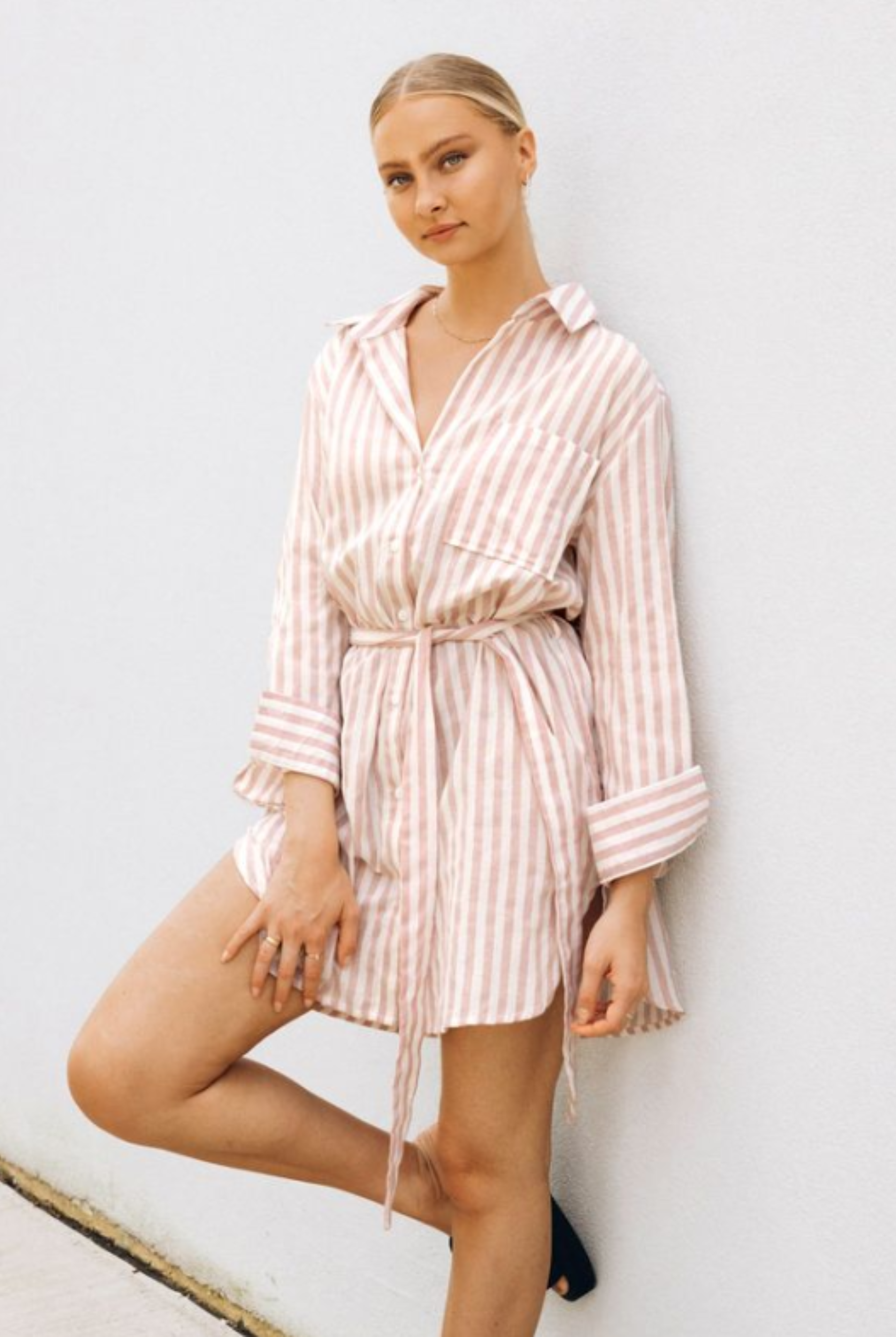 Model wearing soft pink stripe shirt dress with functional button placket, collar and belt