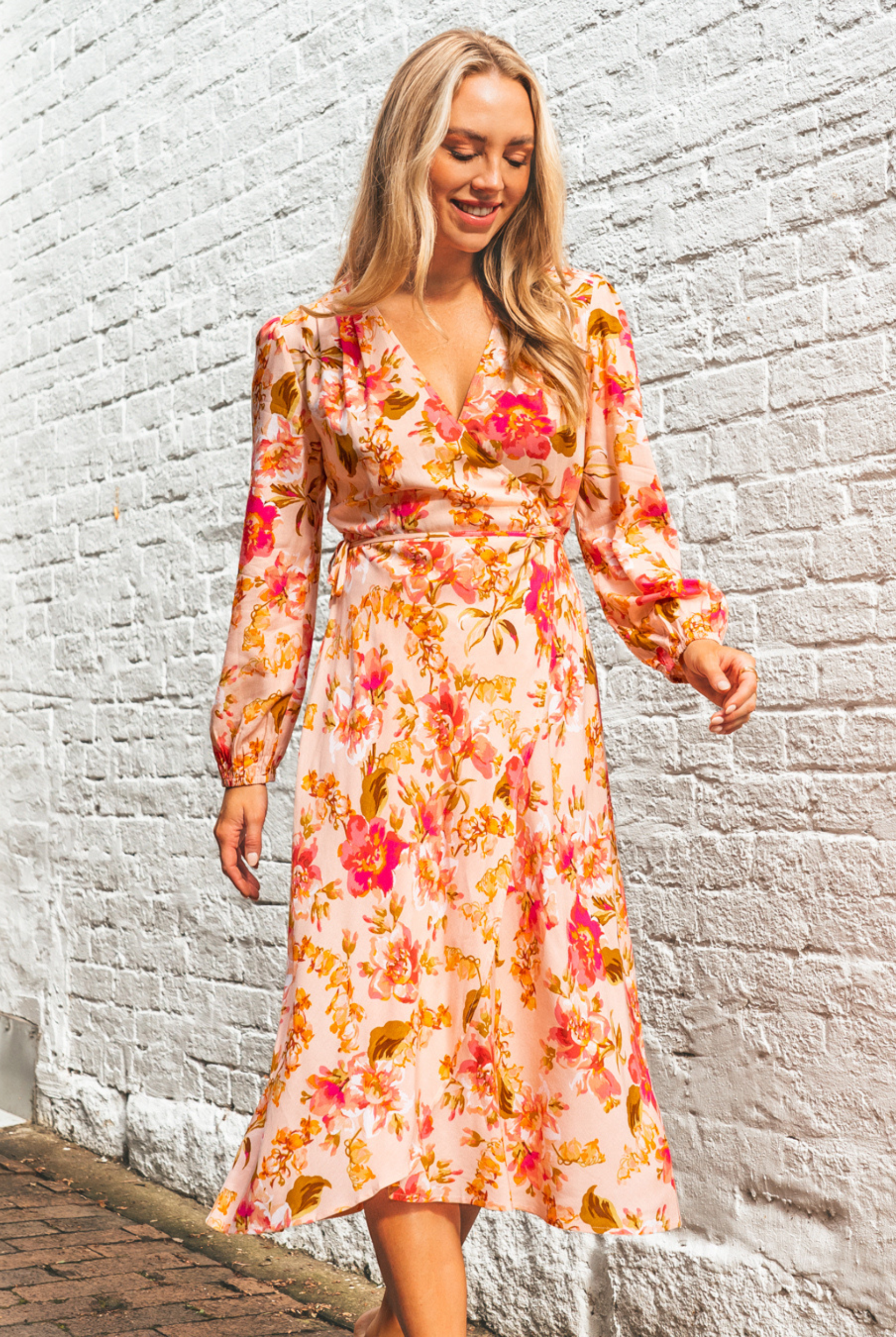Blonde model wearing the Calla Rose Midi Dress in Pink Print with wrap style, long sleeve and tie waist