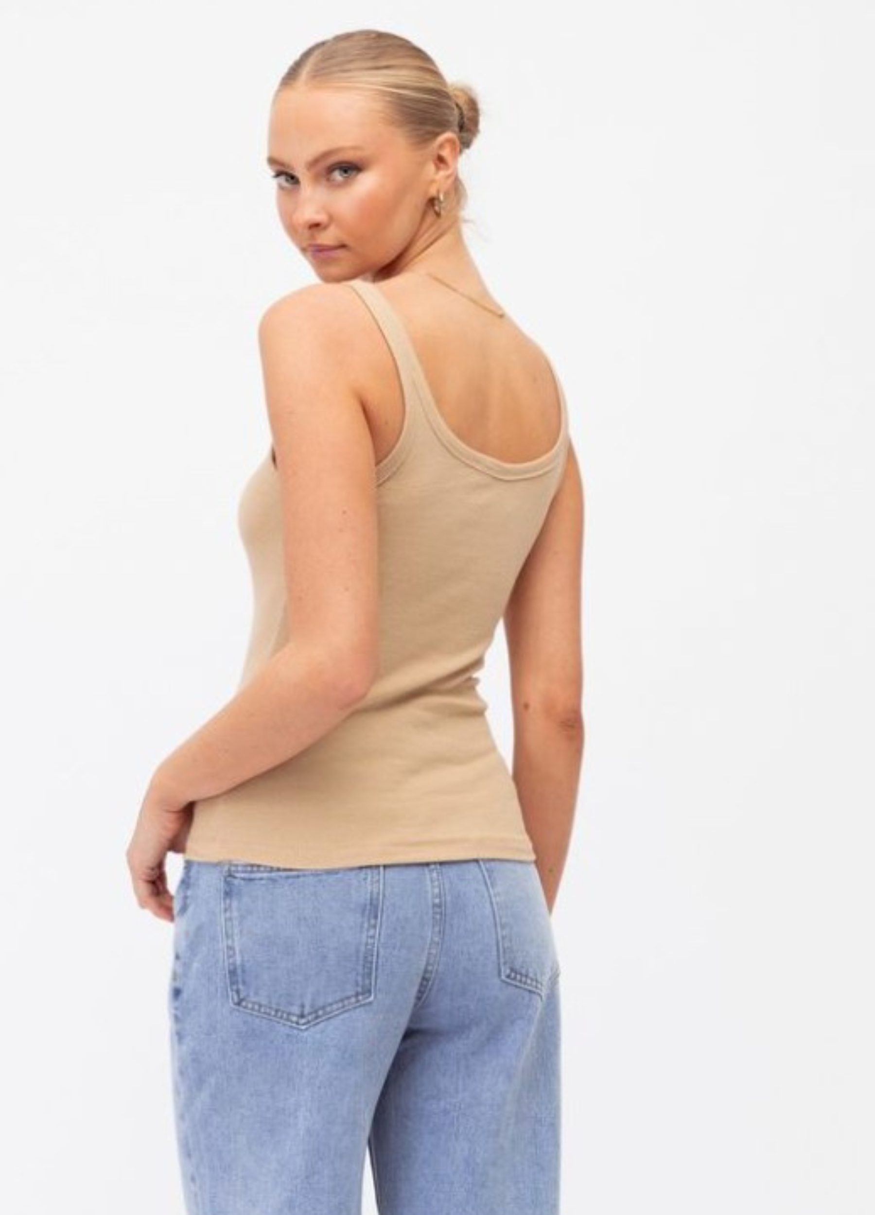 Model wearing a neutral tank with lightwash denim jeans