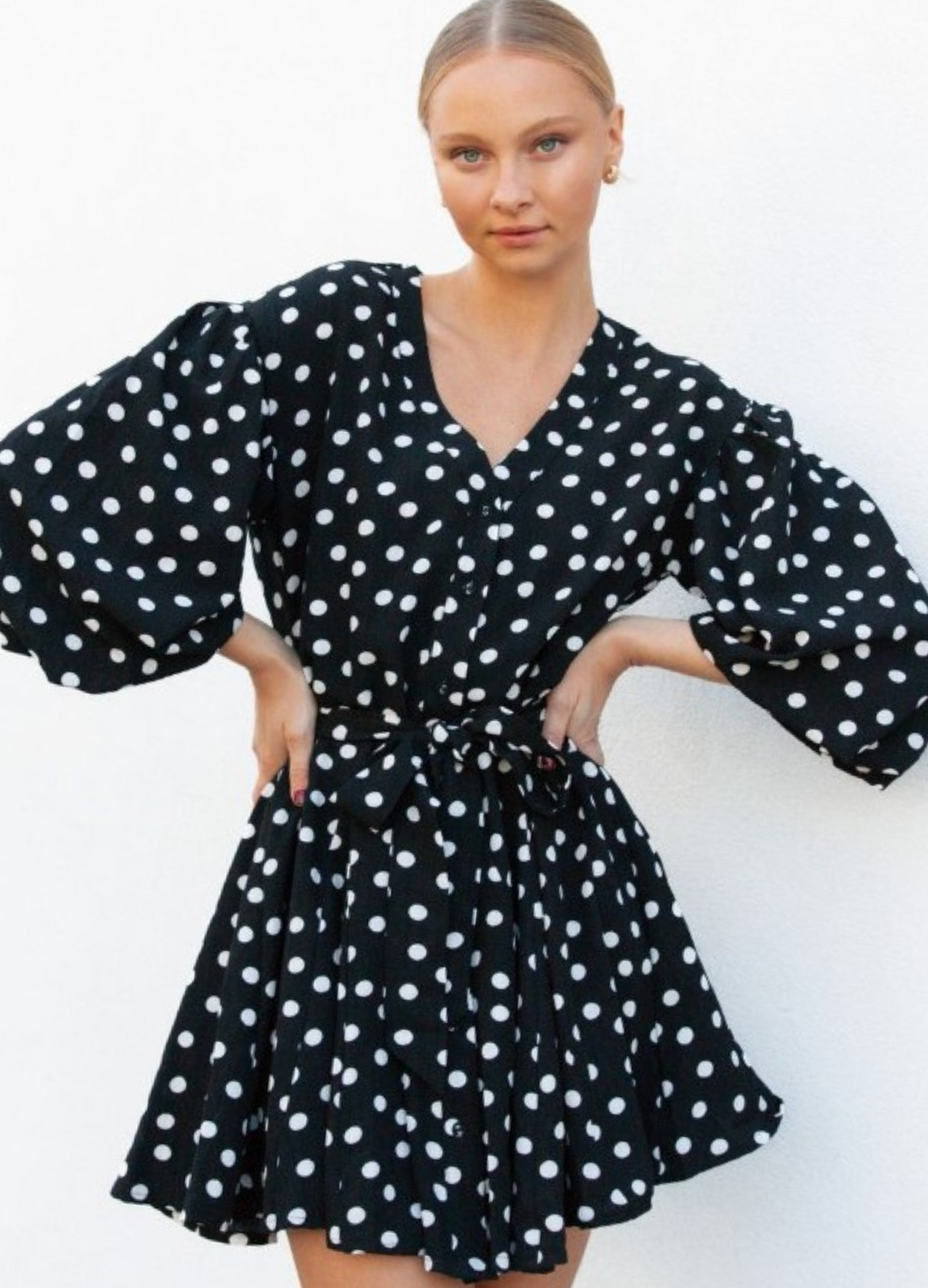 Model wearing black and white polka dot dress with waist belt and buttons