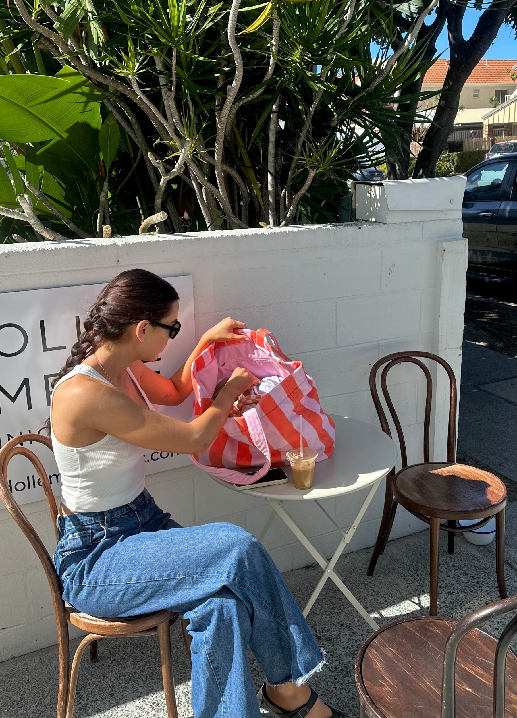 Woman sitting at a table outdoors, opening a pink bag.