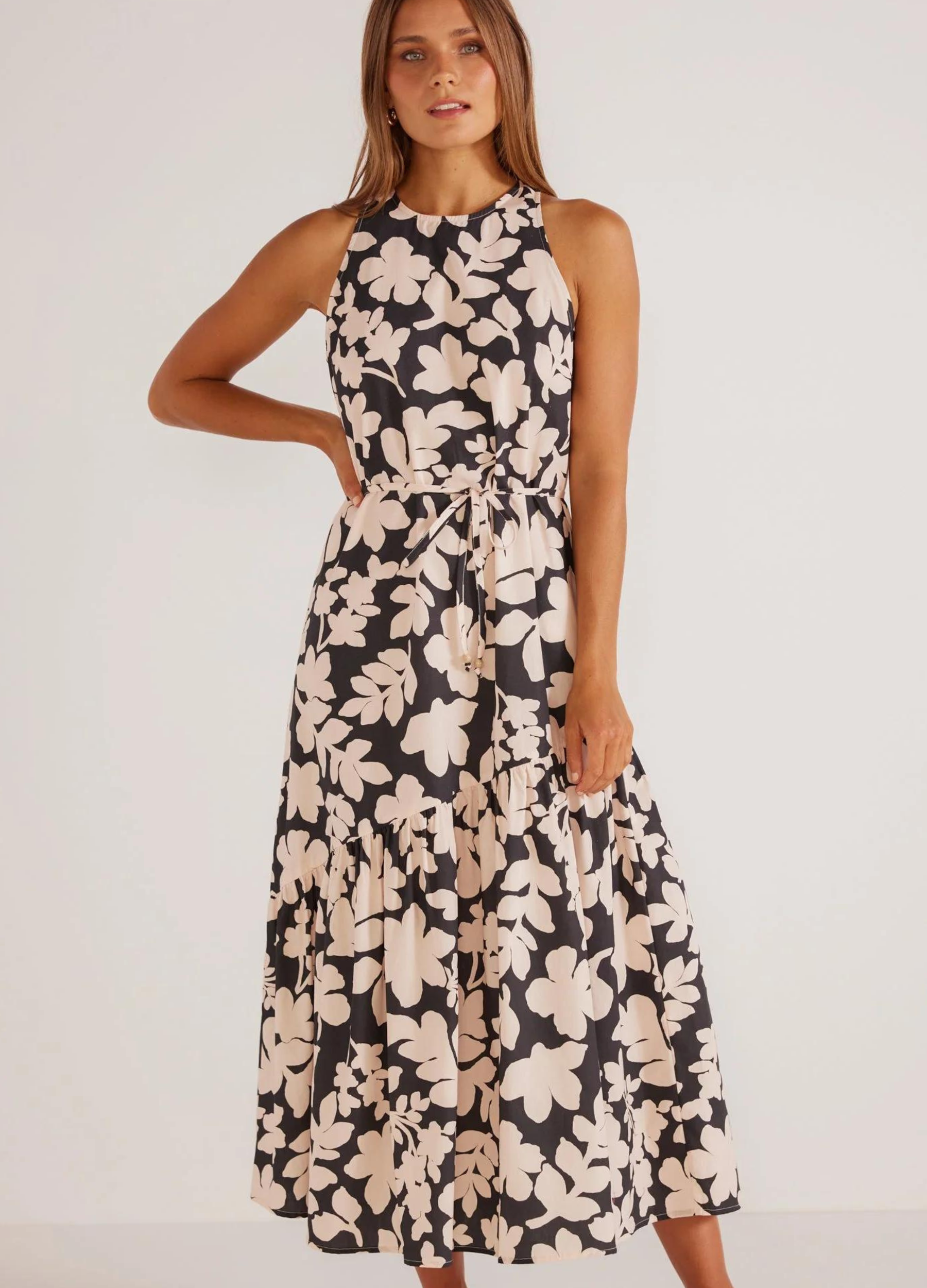 A sleeveless, midi-length dress with a floral print in beige and black, featuring a racer cut neckline, A-line silhouette, and side pockets.