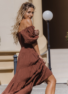 Model wearing chocolate brown tiered dress with short puffy sleeves