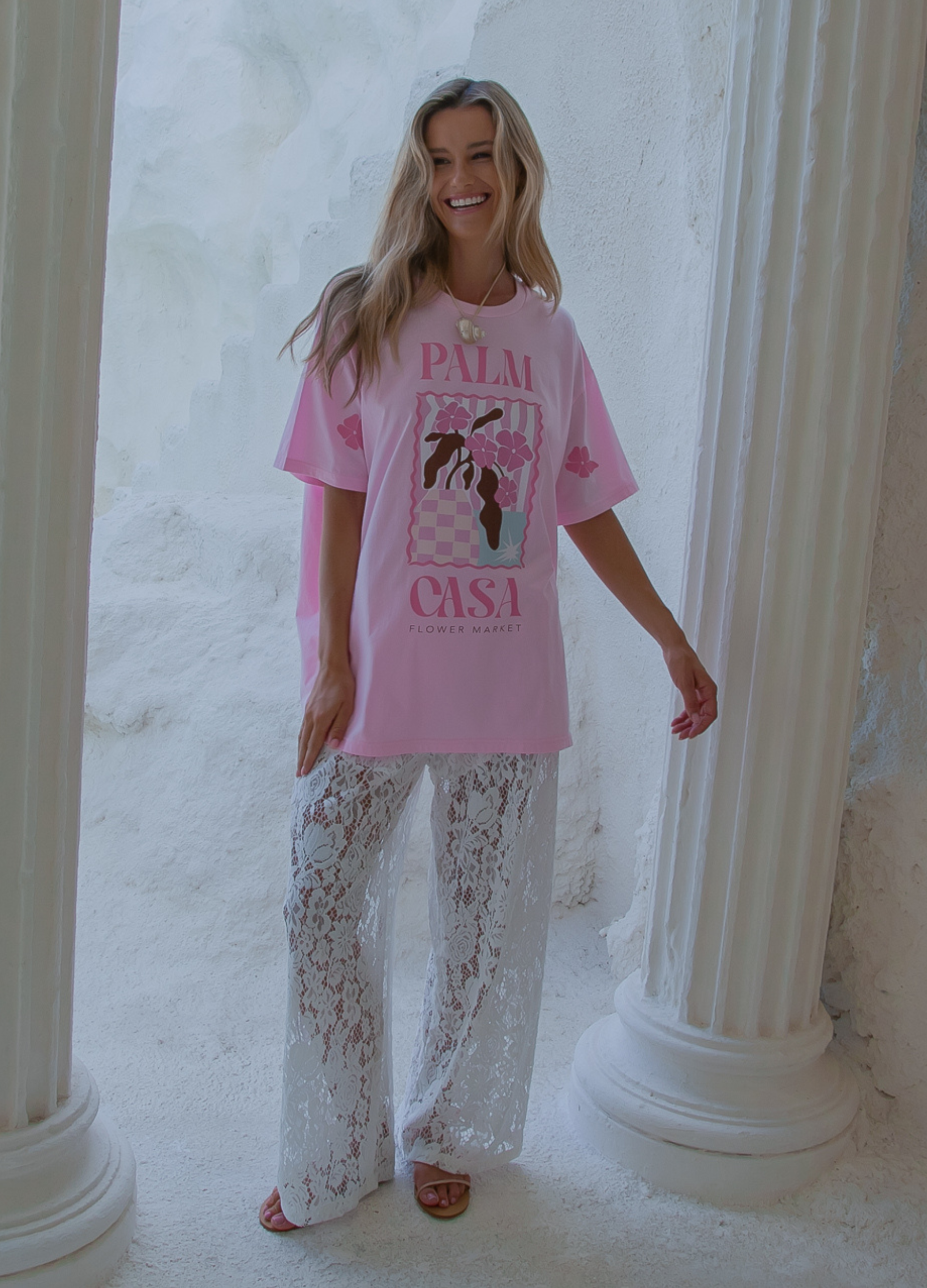 Woman wearing a pink t-shirt with graphics and text, standing in a classical architecture setting.