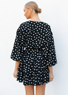 Model wearing black and white polka dot dress with waist belt and buttons