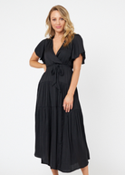 Model wearing black tiered wrap dress with sash belt