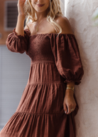 Model wearing chocolate brown tiered dress with short puffy sleeves