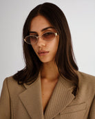 Woman wearing sunglasses and a beige blazer against a plain background
