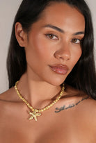 Woman wearing a gold necklace with a starfish pendant against a neutral background