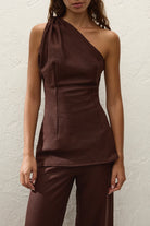 Woman wearing a brown one-shoulder top and pants against a white background