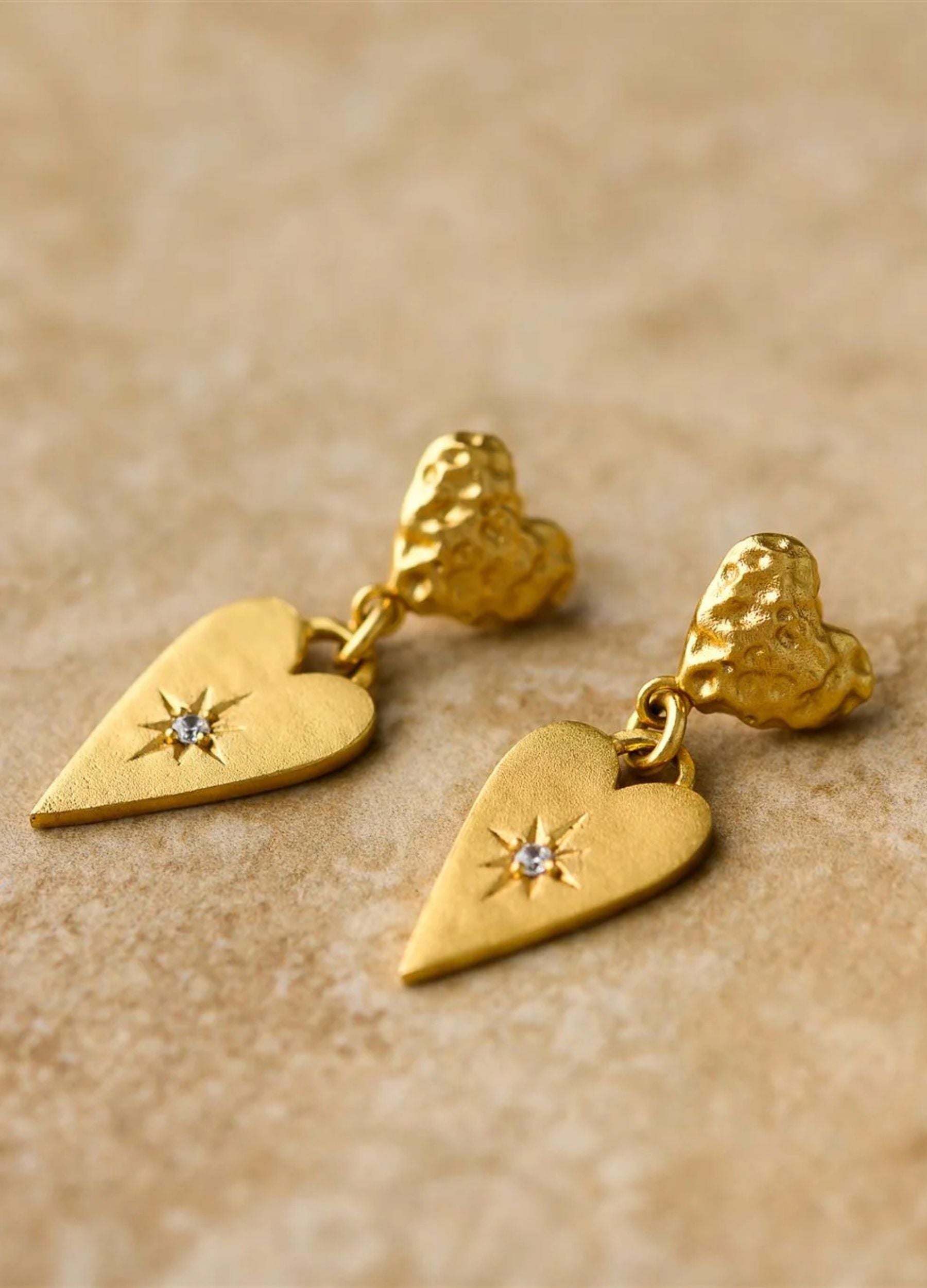 Gold heart-shaped earrings with star details on a beige background
