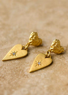 Gold heart-shaped earrings with star details on a beige background