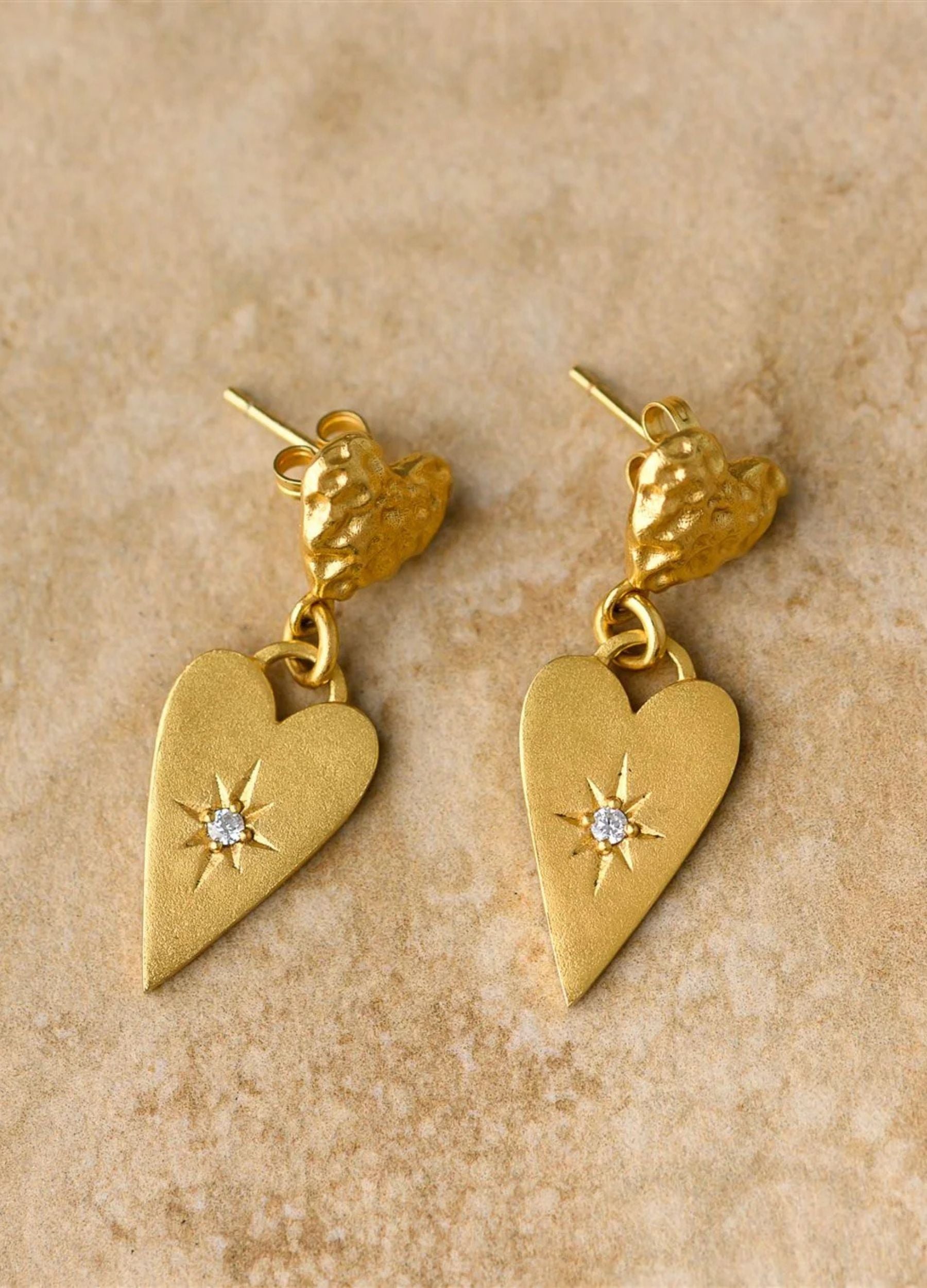 Gold heart-shaped earrings with star details on a beige background