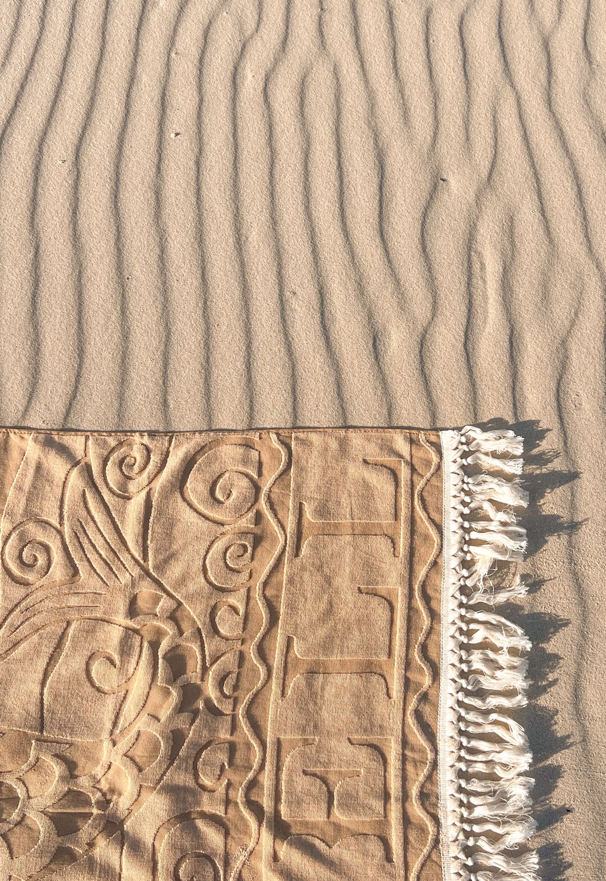 Textured sand surface with a beach towel featuring intricate patterns and fringes.