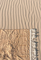 Textured sand surface with a beach towel featuring intricate patterns and fringes.