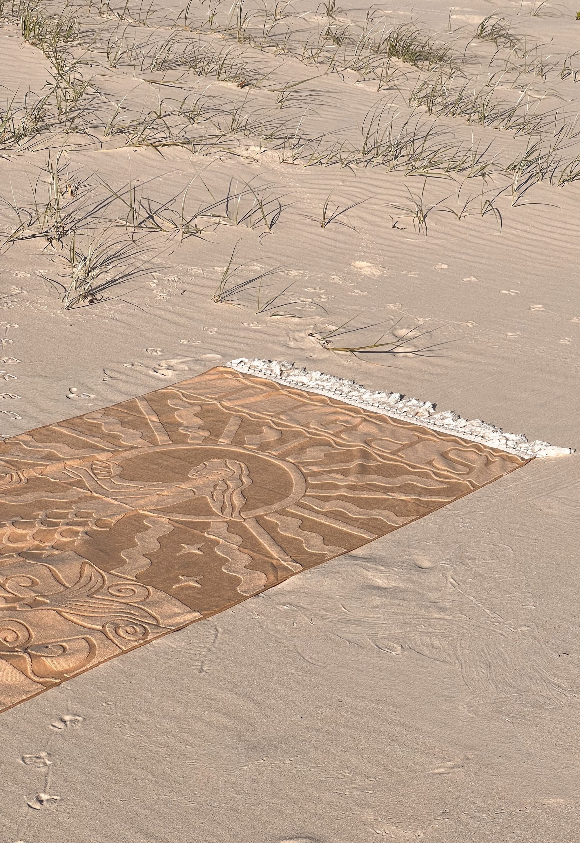 Brown beach towel with intricate patterns on a sandy surface