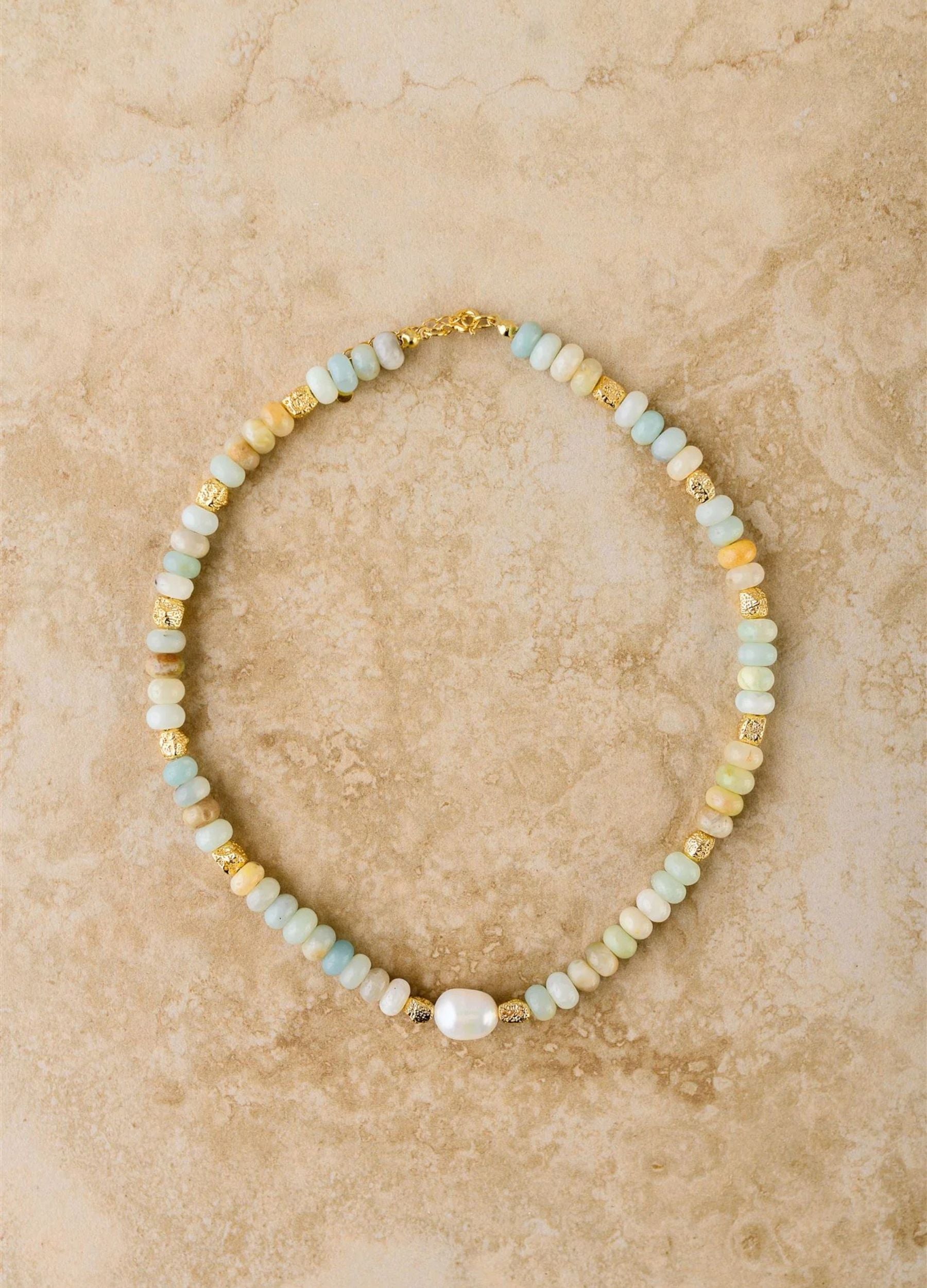 Beaded necklace with gold and pearl accents on a beige marble background